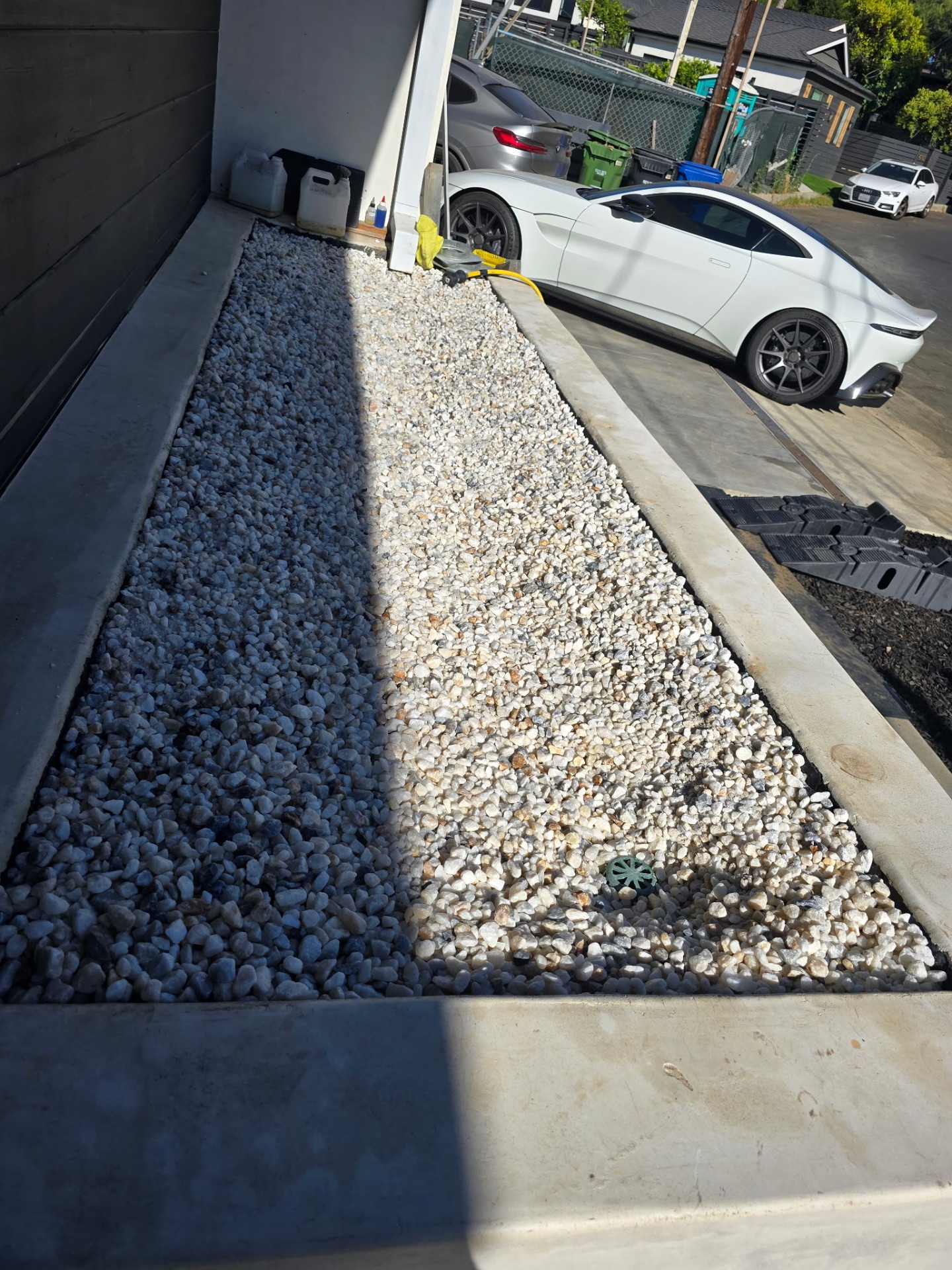 Washed-stone side-yard planter, crisp against the driveway